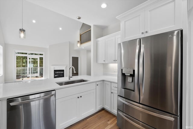 kitchen with pendant lighting, sink, white cabinetry, appliances with stainless steel finishes, and vaulted ceiling