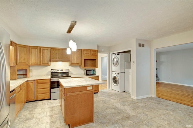 kitchen with a textured ceiling, stacked washer / dryer, a kitchen island, appliances with stainless steel finishes, and decorative light fixtures