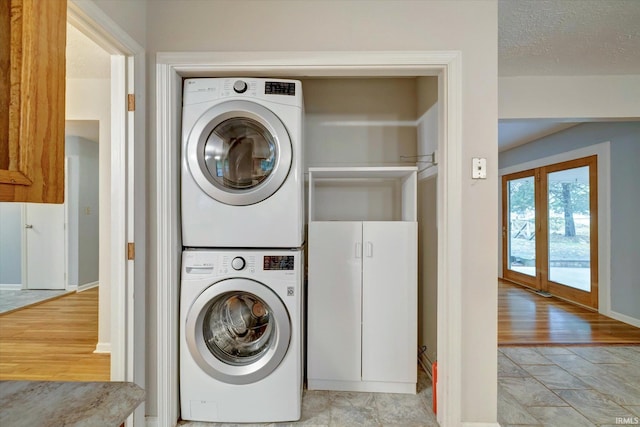 laundry area with light hardwood / wood-style flooring, a textured ceiling, and stacked washer and clothes dryer