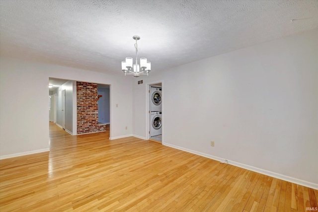 unfurnished room featuring an inviting chandelier, a textured ceiling, light hardwood / wood-style floors, and stacked washing maching and dryer