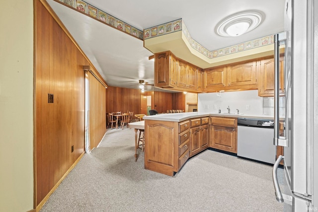 kitchen featuring a breakfast bar area, wood walls, kitchen peninsula, ceiling fan, and stainless steel dishwasher