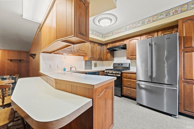 kitchen featuring wood walls, sink, kitchen peninsula, appliances with stainless steel finishes, and a kitchen breakfast bar