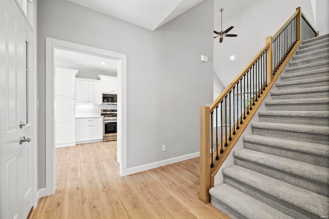 stairway with a high ceiling, ceiling fan, and hardwood / wood-style floors