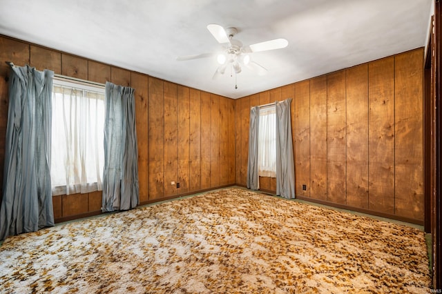 empty room with carpet flooring, ceiling fan, and wood walls