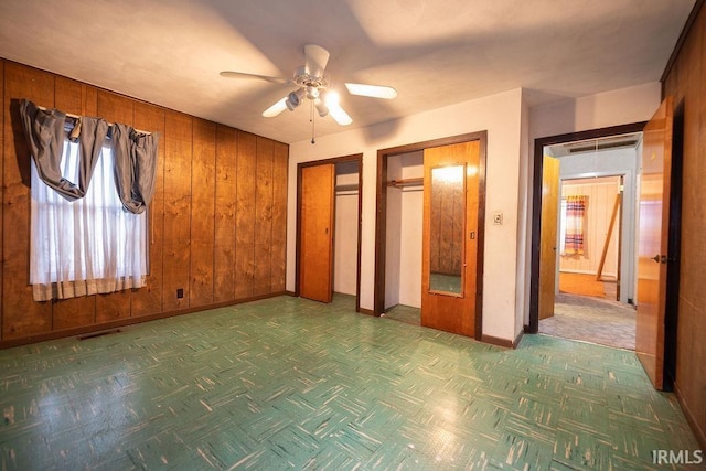 unfurnished bedroom featuring parquet flooring, multiple closets, ceiling fan, and wooden walls