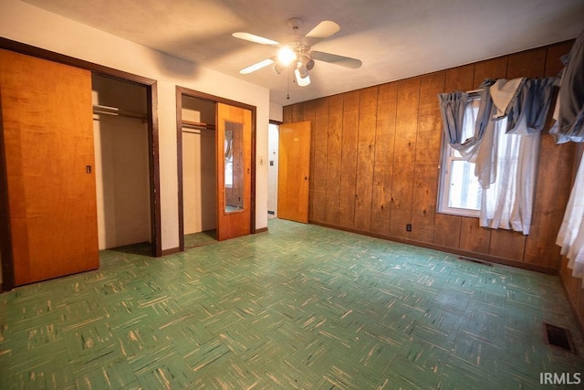 unfurnished bedroom with multiple closets, ceiling fan, and wooden walls