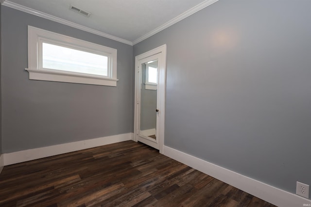 empty room with crown molding, baseboards, dark wood-style floors, and visible vents