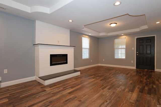 unfurnished living room with a glass covered fireplace, a raised ceiling, baseboards, and dark wood-style floors