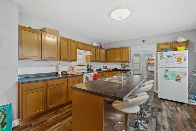 kitchen with sink, dark wood-type flooring, a kitchen breakfast bar, an island with sink, and white appliances