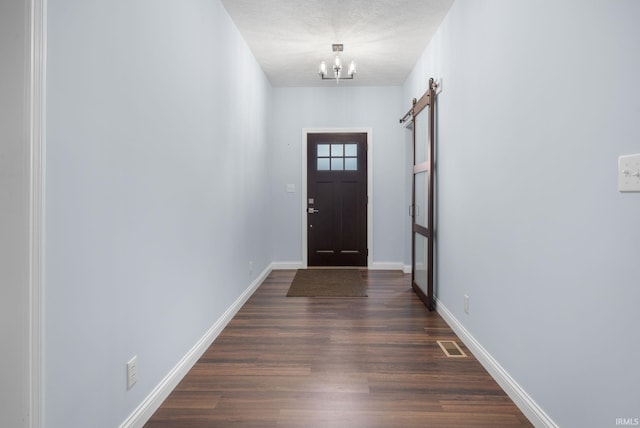 entryway featuring dark hardwood / wood-style flooring, a textured ceiling, an inviting chandelier, and a barn door