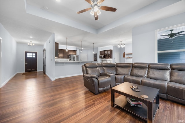 living room with ceiling fan with notable chandelier, a tray ceiling, and dark hardwood / wood-style flooring