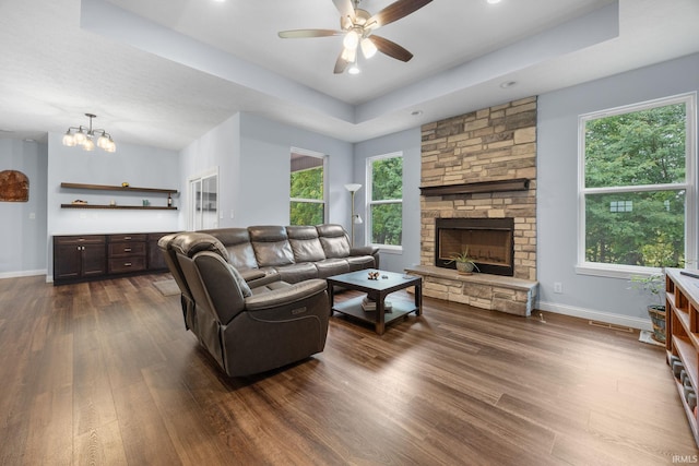 living room featuring ceiling fan with notable chandelier, a fireplace, dark hardwood / wood-style floors, and a tray ceiling