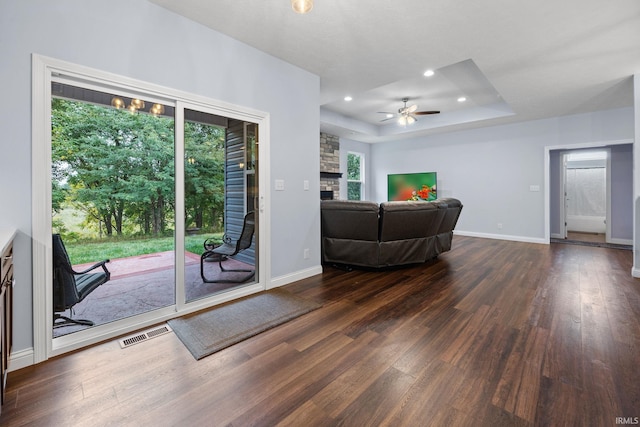 living room featuring a raised ceiling, a stone fireplace, dark hardwood / wood-style flooring, and ceiling fan