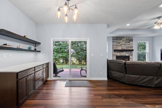 interior space featuring dark brown cabinets, dark hardwood / wood-style floors, ceiling fan with notable chandelier, a fireplace, and a raised ceiling