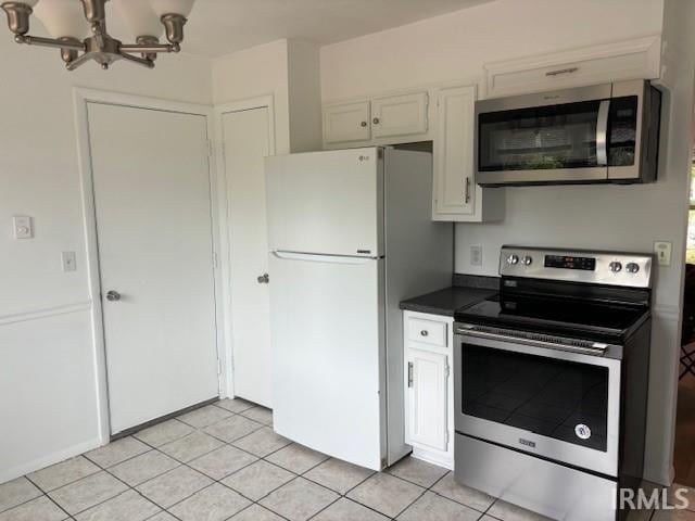 kitchen with an inviting chandelier, stainless steel appliances, white cabinets, and light tile patterned floors