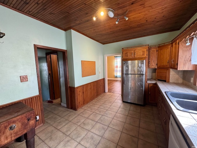 kitchen with dishwashing machine, stainless steel fridge, wood ceiling, tile counters, and wooden walls