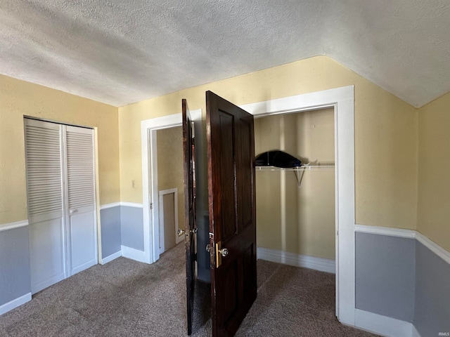 unfurnished bedroom featuring a closet, vaulted ceiling, a textured ceiling, and carpet floors