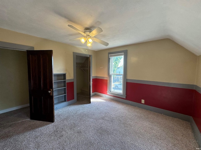 unfurnished bedroom featuring vaulted ceiling, a spacious closet, carpet floors, a textured ceiling, and ceiling fan