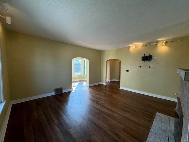 unfurnished living room with a textured ceiling and dark hardwood / wood-style flooring