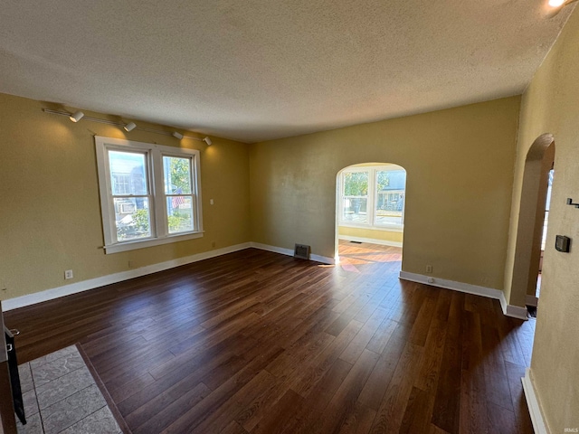 spare room with a wealth of natural light, a textured ceiling, and dark hardwood / wood-style flooring