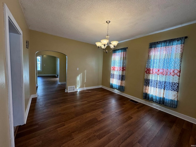 unfurnished room with an inviting chandelier, a textured ceiling, dark hardwood / wood-style floors, and plenty of natural light