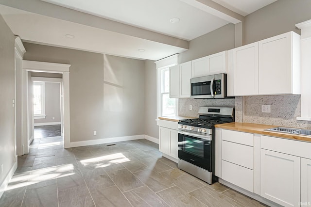 kitchen with white cabinets, stainless steel appliances, tasteful backsplash, and wooden counters