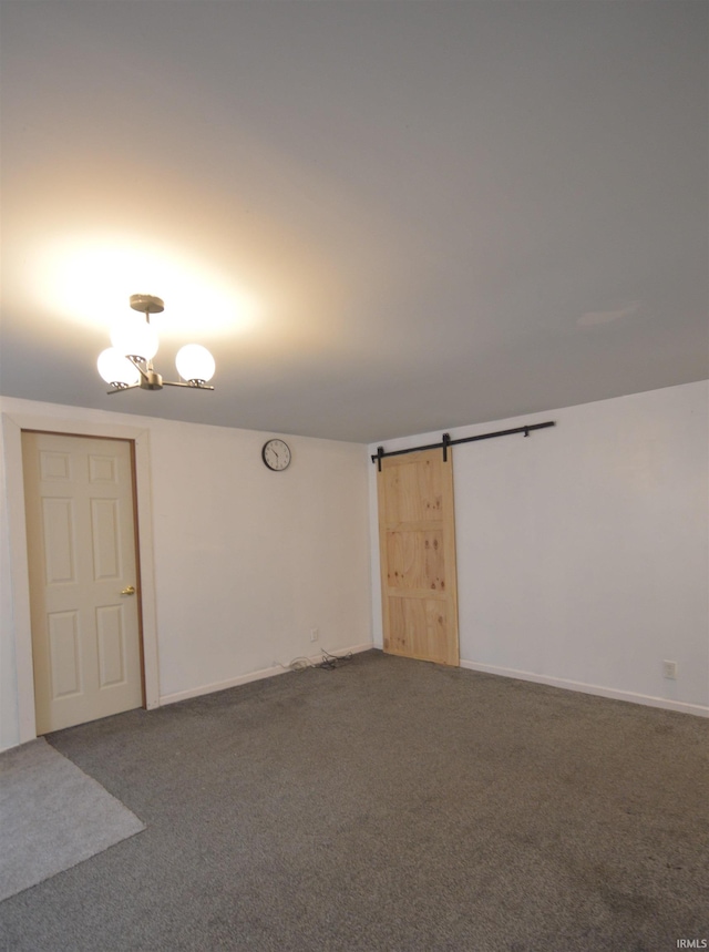 empty room featuring a barn door, dark carpet, and a chandelier