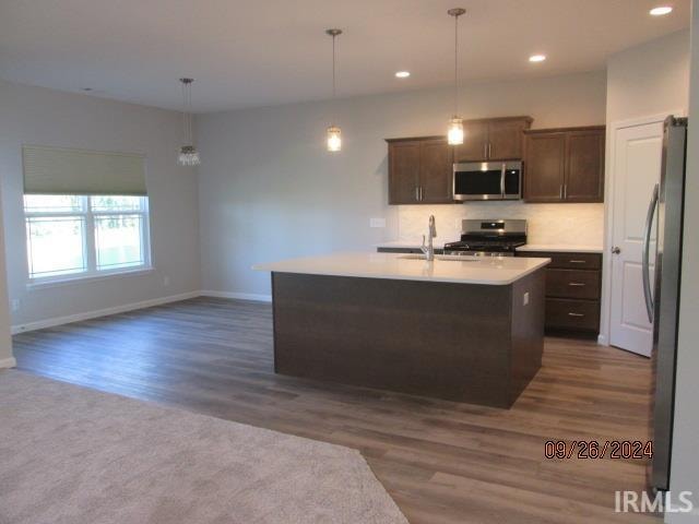 kitchen featuring hanging light fixtures, dark wood-type flooring, stainless steel appliances, dark brown cabinets, and a center island with sink