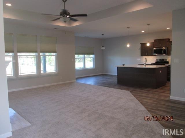 kitchen featuring pendant lighting, stainless steel appliances, ceiling fan, dark carpet, and a center island with sink