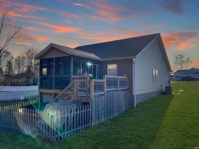 back house at dusk featuring a sunroom, cooling unit, and a yard