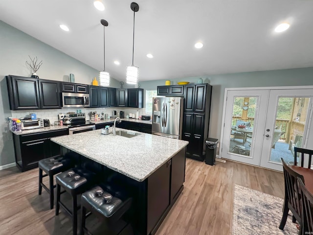 kitchen featuring lofted ceiling, sink, decorative light fixtures, a center island with sink, and stainless steel appliances