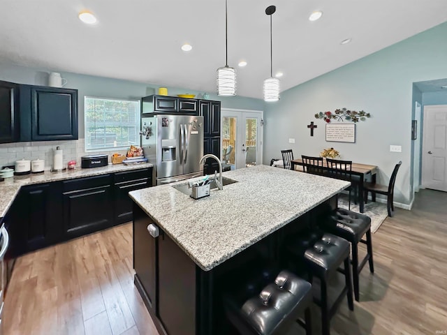 kitchen featuring pendant lighting, a kitchen island with sink, sink, stainless steel refrigerator with ice dispenser, and light hardwood / wood-style flooring