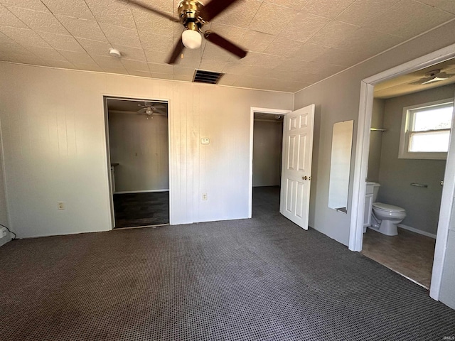 unfurnished bedroom featuring dark carpet, a closet, ceiling fan, and ensuite bathroom