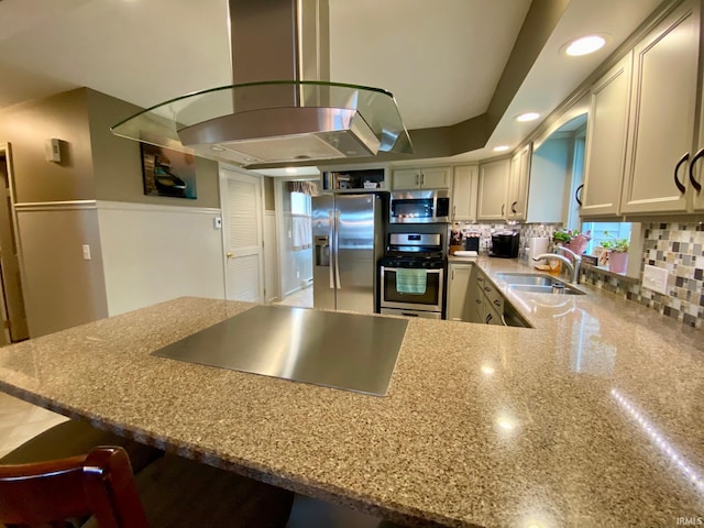 kitchen with light stone counters, sink, kitchen peninsula, island range hood, and appliances with stainless steel finishes