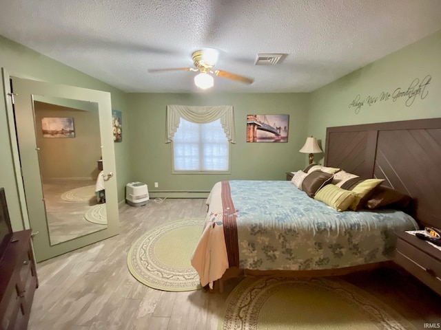 bedroom with a textured ceiling, light hardwood / wood-style floors, a baseboard heating unit, and ceiling fan