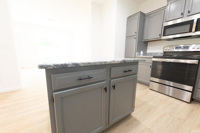 kitchen featuring light stone countertops, light wood-type flooring, stainless steel appliances, gray cabinetry, and a center island