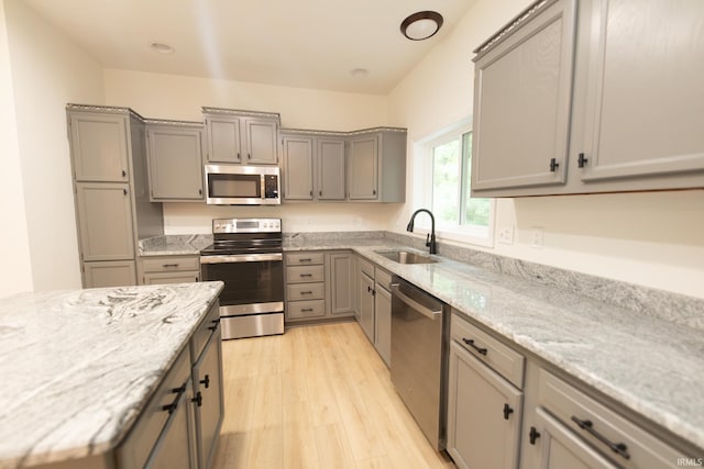 kitchen with light hardwood / wood-style floors, stainless steel appliances, sink, and gray cabinetry