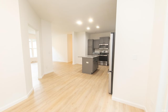 kitchen with light stone countertops, a center island, light hardwood / wood-style floors, stainless steel appliances, and gray cabinets