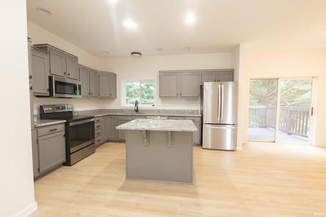 kitchen featuring a kitchen island, light hardwood / wood-style flooring, gray cabinetry, sink, and appliances with stainless steel finishes