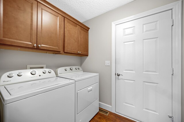 clothes washing area featuring a textured ceiling, washing machine and dryer, dark wood-type flooring, and cabinets