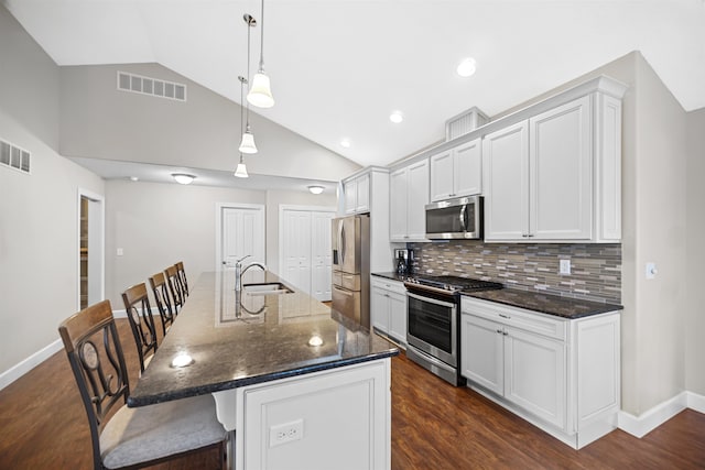 kitchen with a breakfast bar, dark hardwood / wood-style floors, a center island with sink, appliances with stainless steel finishes, and decorative light fixtures