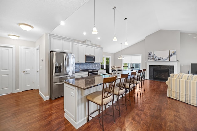 kitchen with a kitchen island with sink, white cabinetry, stainless steel appliances, a breakfast bar, and a fireplace