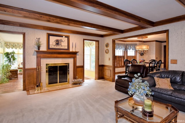 living room featuring beamed ceiling, a notable chandelier, a tiled fireplace, light colored carpet, and crown molding