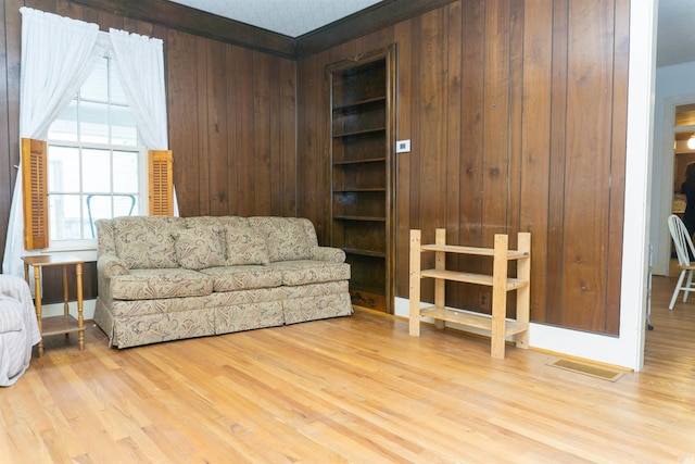 living area featuring light wood-type flooring, wood walls, and crown molding