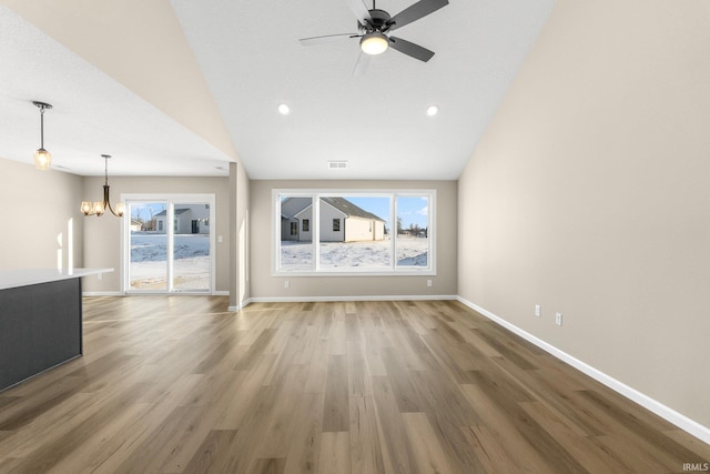 unfurnished living room featuring hardwood / wood-style flooring, lofted ceiling, and ceiling fan with notable chandelier