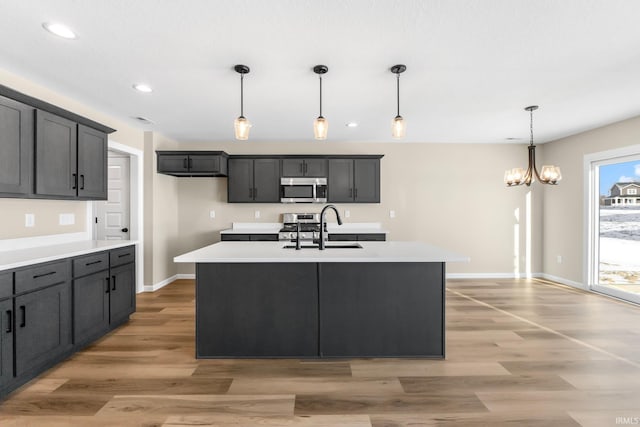 kitchen featuring appliances with stainless steel finishes, hanging light fixtures, sink, and a center island with sink