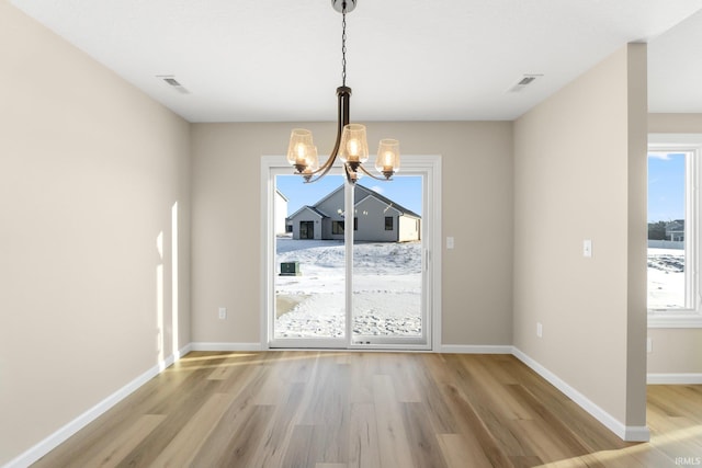 unfurnished dining area featuring light wood-type flooring, a wealth of natural light, and a chandelier