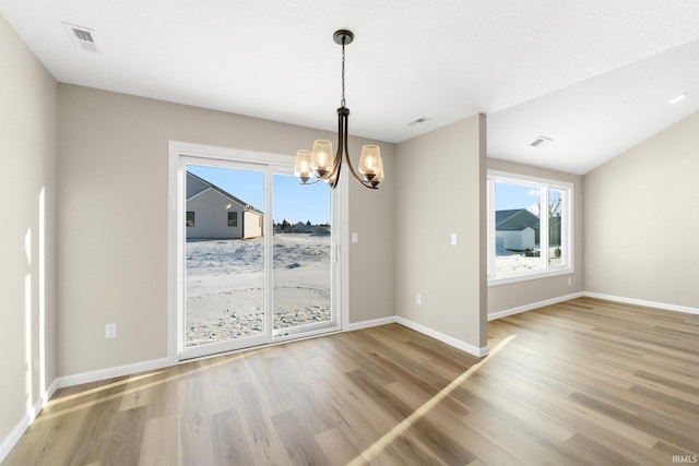 unfurnished dining area with hardwood / wood-style floors, vaulted ceiling, and a chandelier