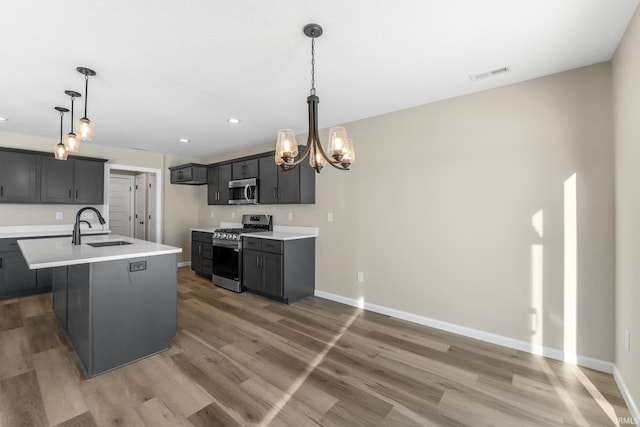 kitchen with dark hardwood / wood-style floors, sink, hanging light fixtures, stainless steel appliances, and a center island with sink