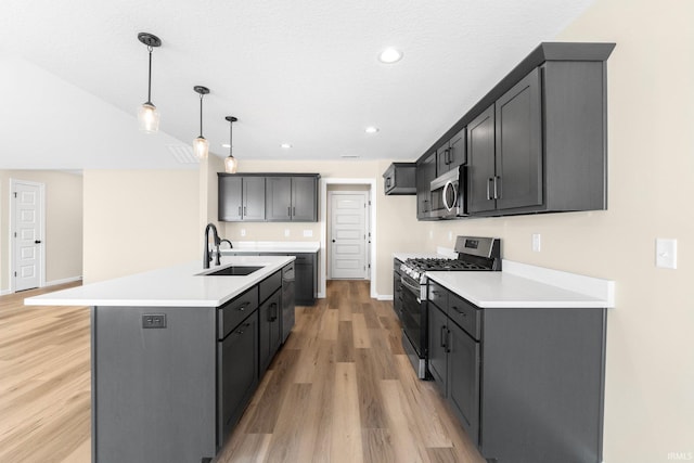 kitchen featuring sink, appliances with stainless steel finishes, a center island with sink, decorative light fixtures, and light wood-type flooring